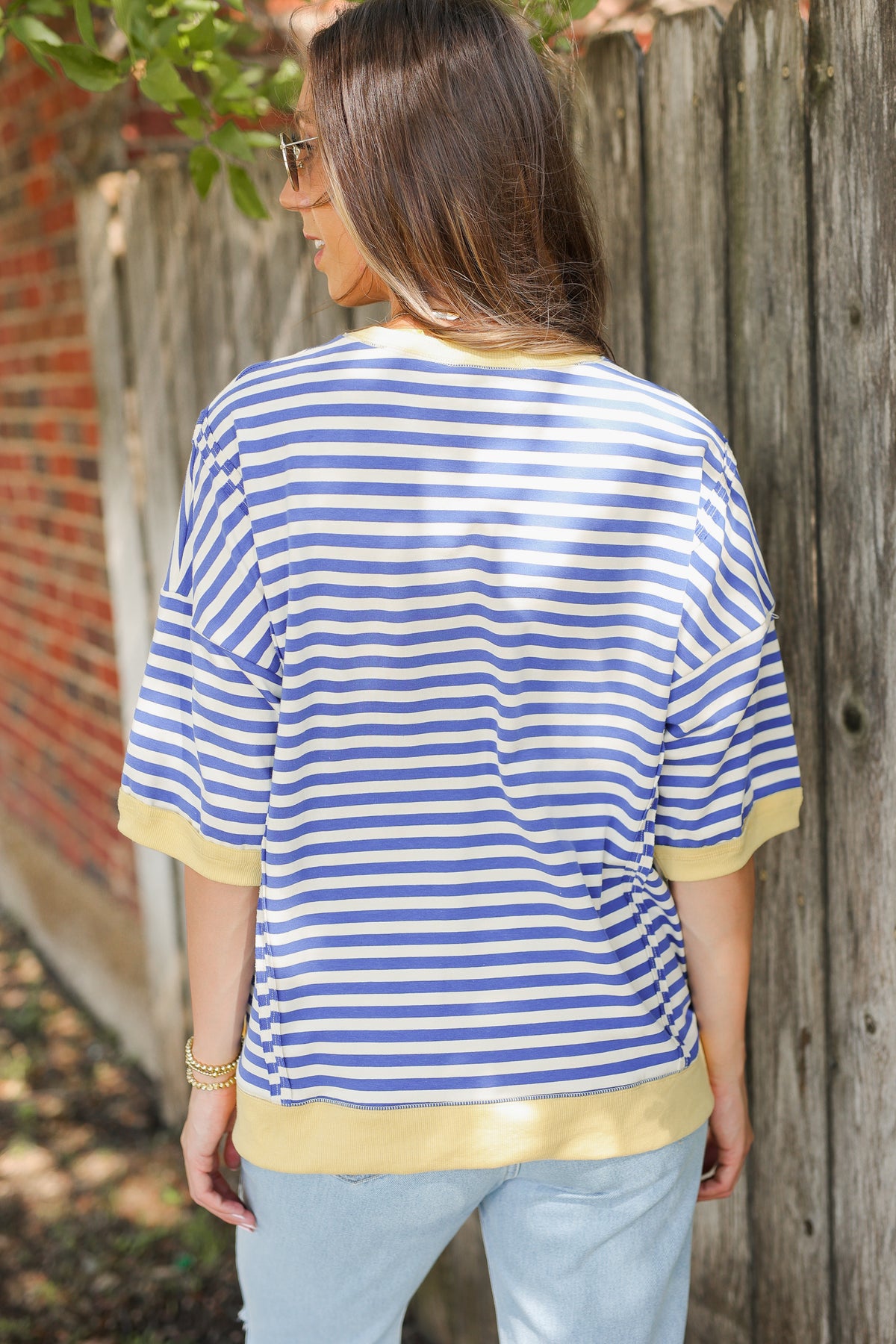 Woman wearing a blue and white striped shirt with yellow trim against a wooden fence.
