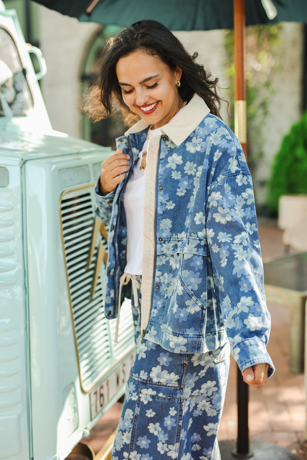 Woman wearing a blue floral denim outfit standing next to a vintage car.