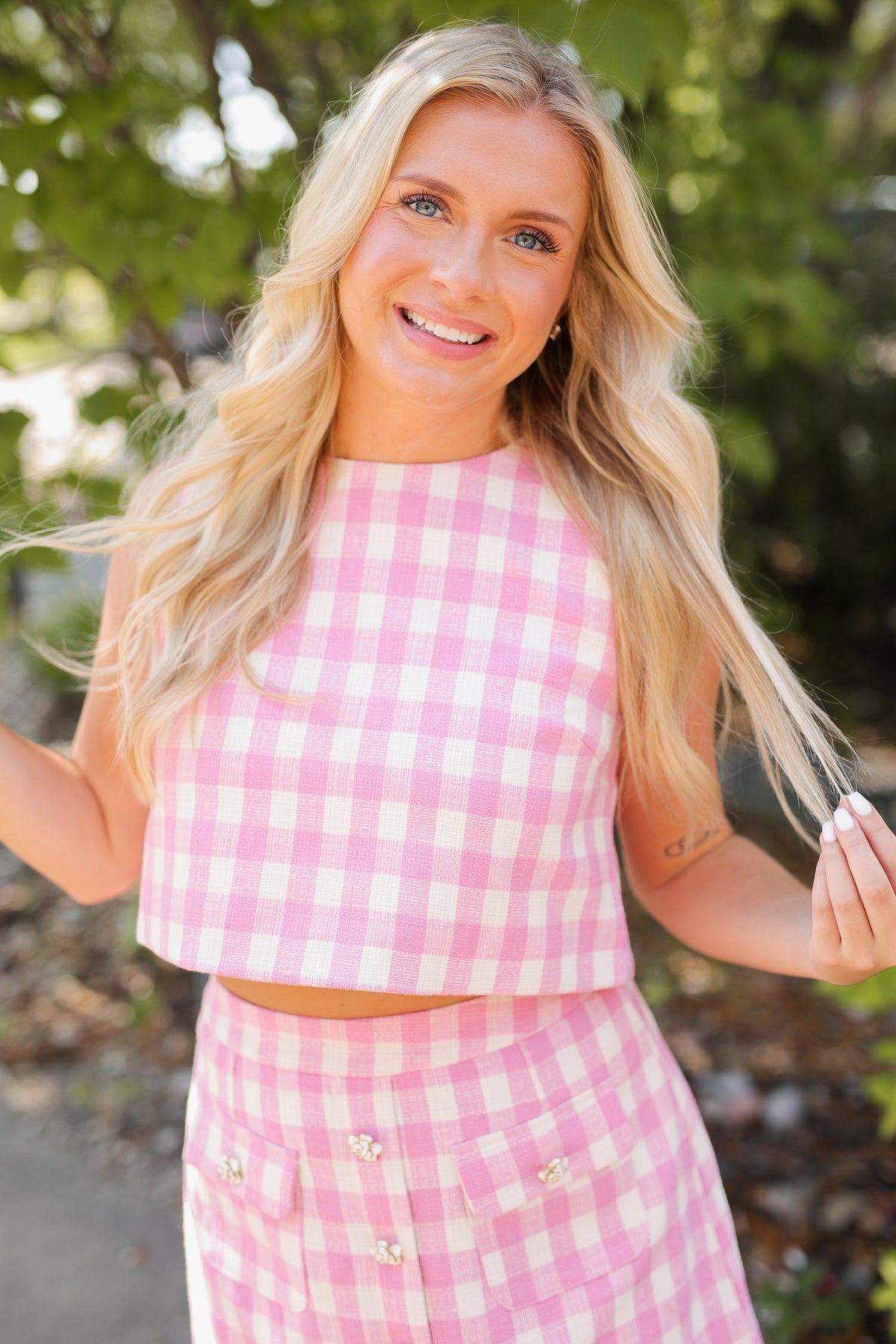 Blonde model wearing a pink and white checkered tank and skirt set in an outdoor setting.