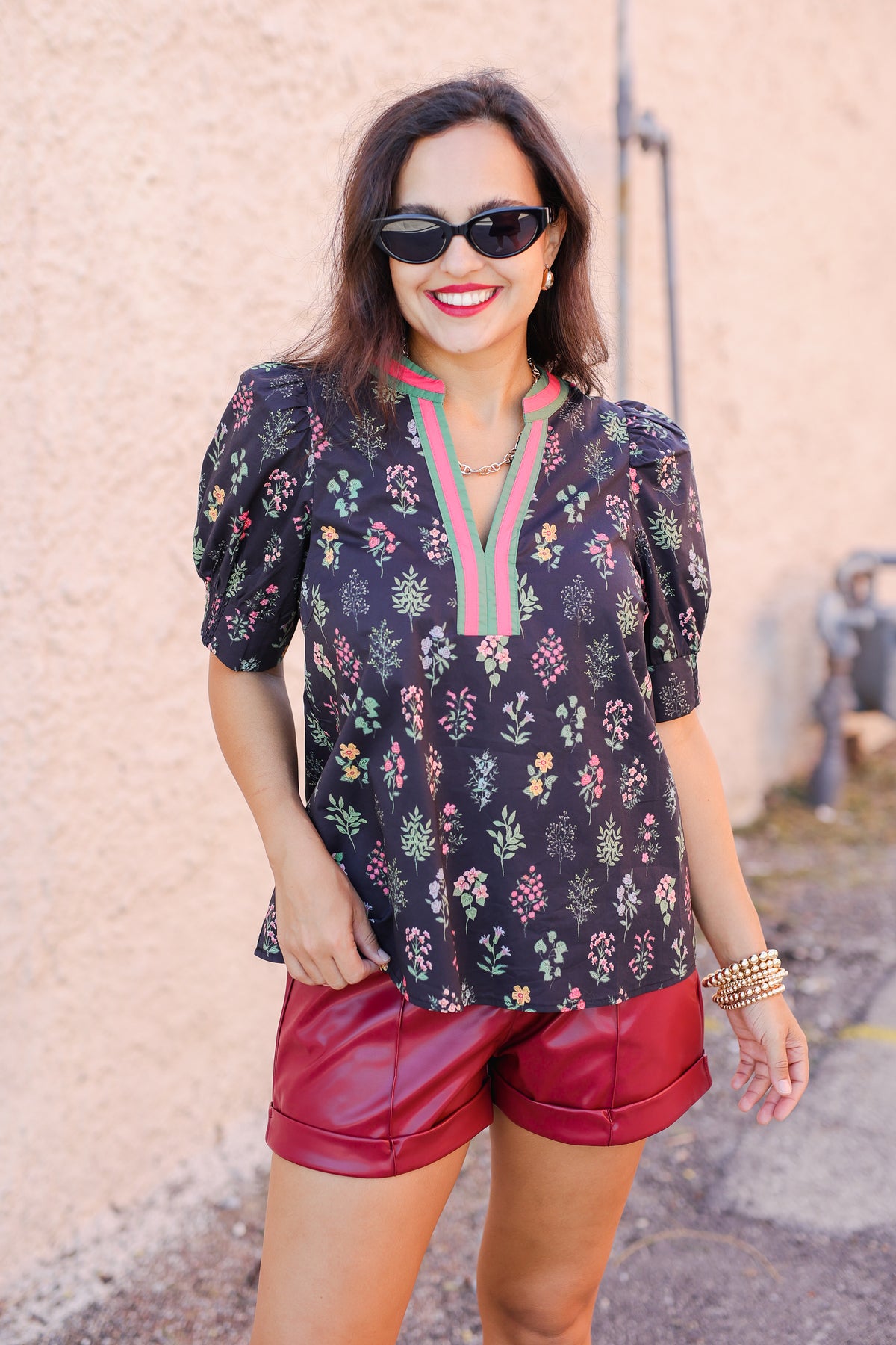 Woman wearing a floral blouse and red shorts against a pink wall.