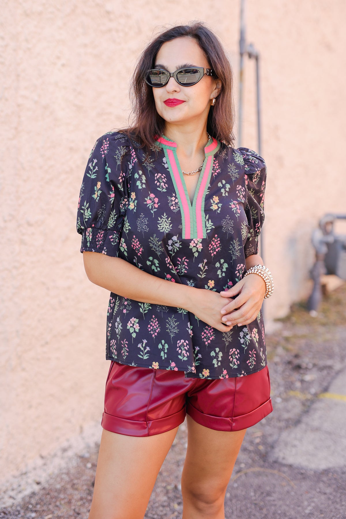 Woman wearing a floral blouse and red shorts against a textured wall.