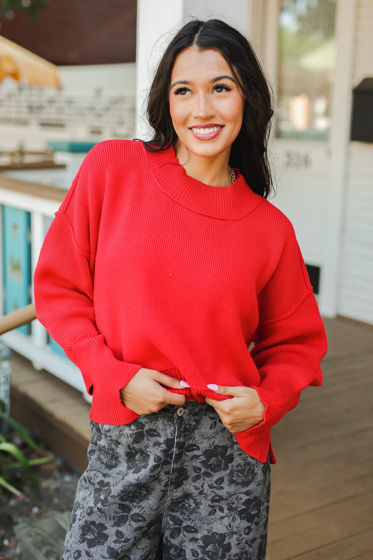 Woman wearing a red sweater and patterned pants standing outdoors.