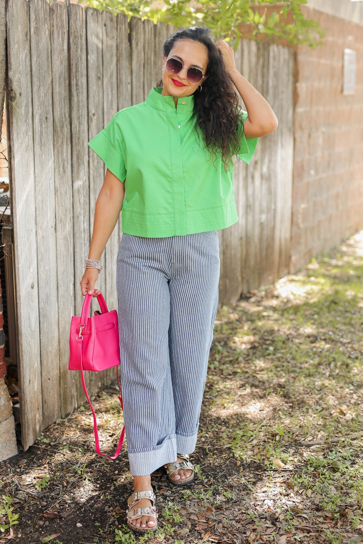 Woman in green shirt and gray pants holding a pink bag outdoors.