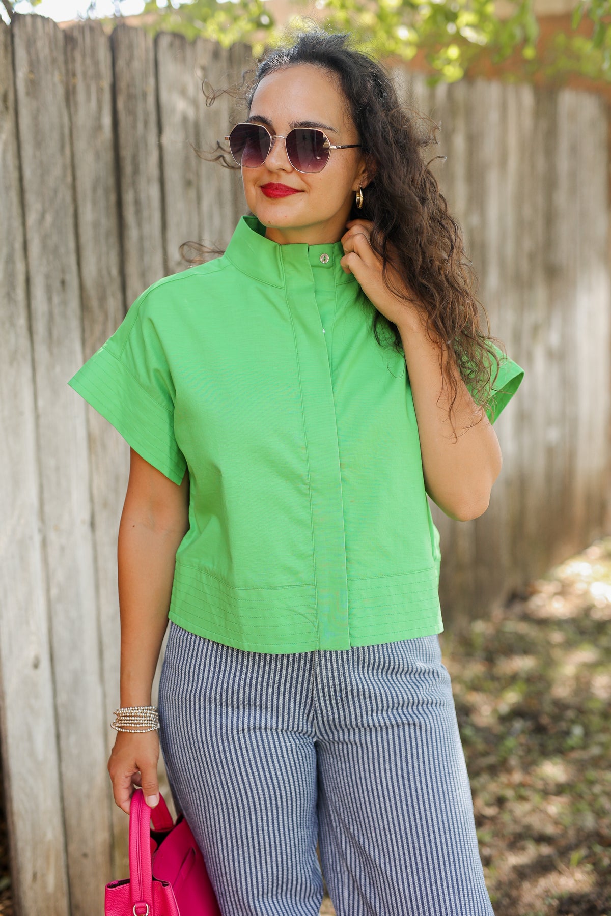 Woman wearing a green sleeveless jacket and gray striped pants, standing outdoors.