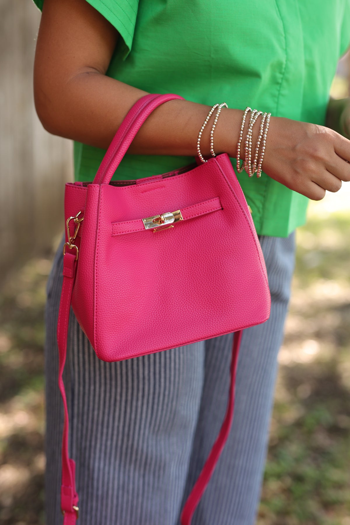 Person holding a pink handbag with a blurred green shirt and gray pants in the background