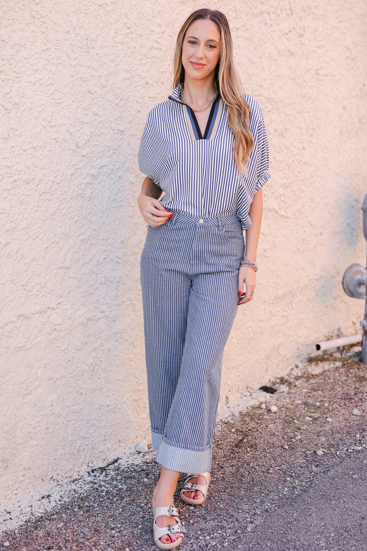 Woman wearing a blue and white striped outfit against a textured wall.