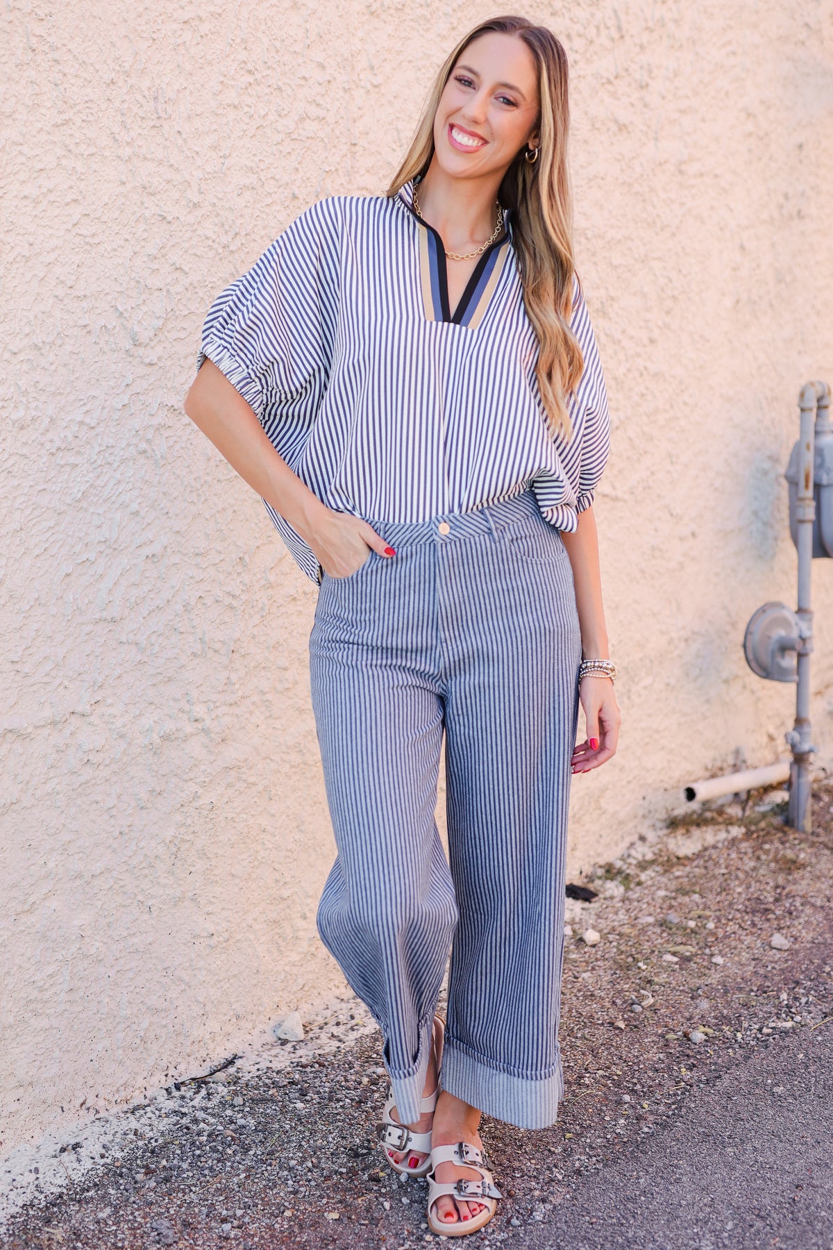 Woman wearing a blue and white striped outfit standing against a beige wall.