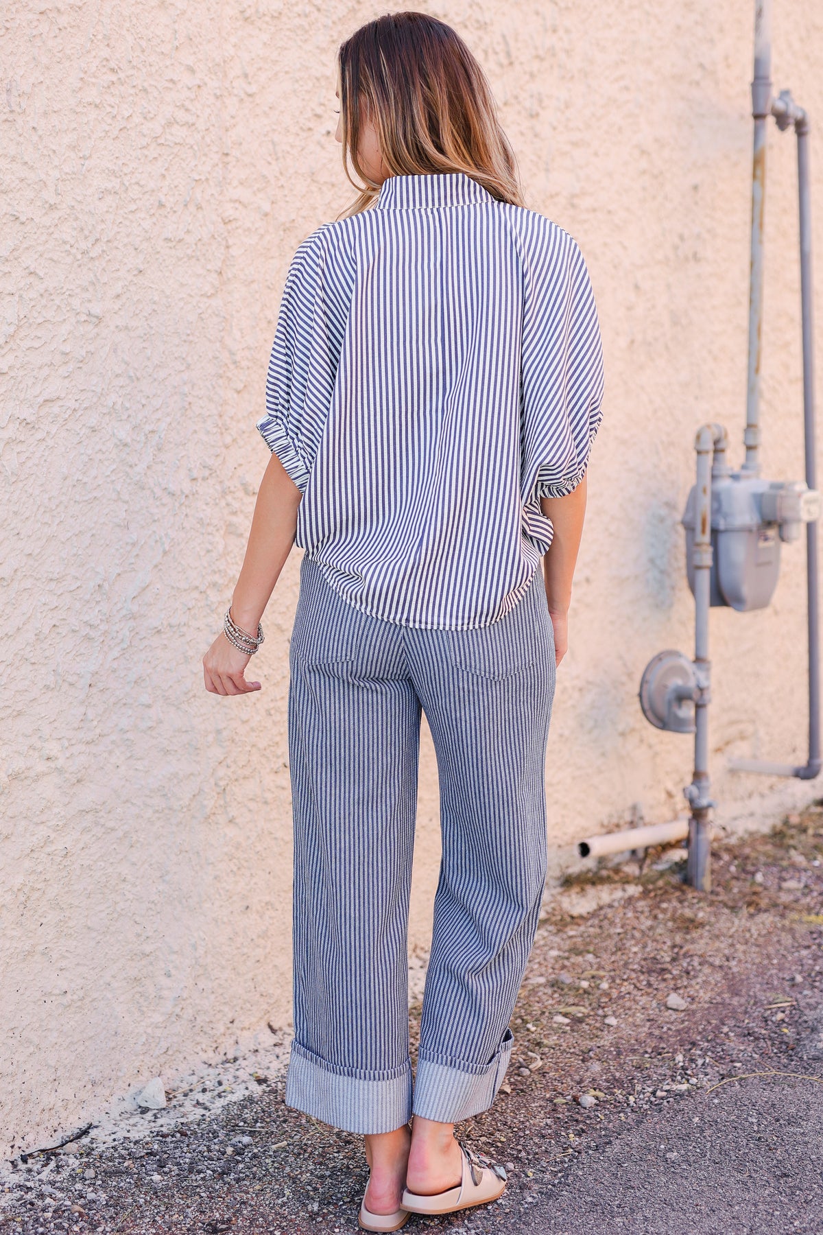 Person wearing a blue and white striped shirt and pants against a beige wall.