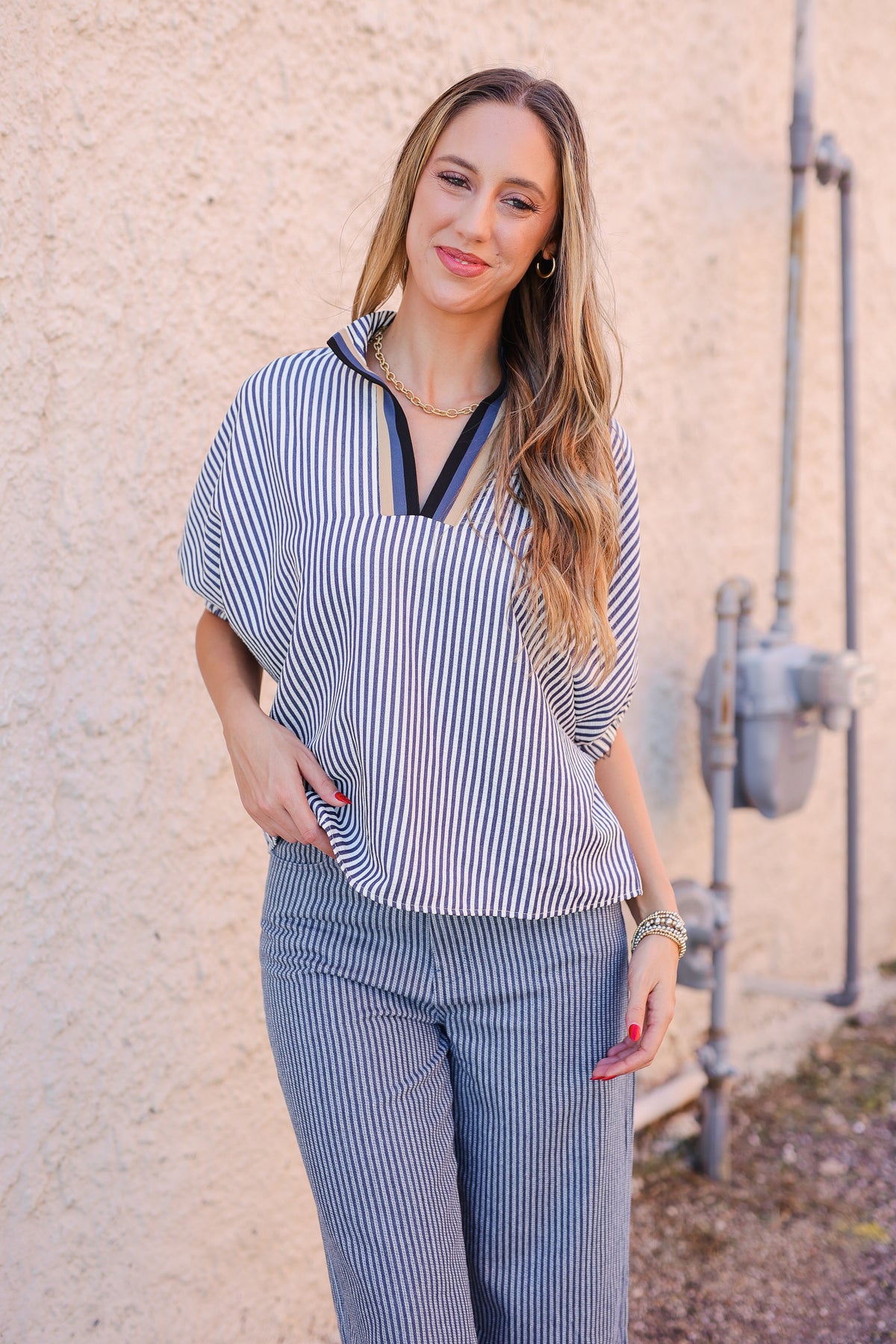 Woman wearing a blue and white striped outfit standing against a beige wall.