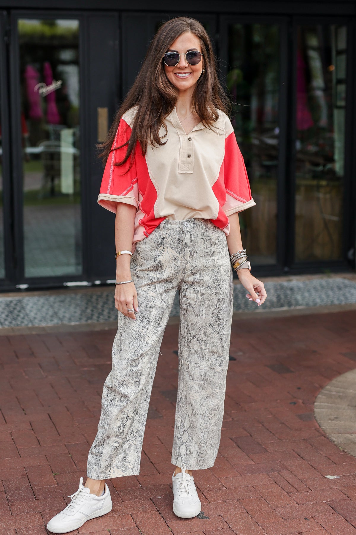 Woman wearing a red and beige top with patterned pants on a brick sidewalk.