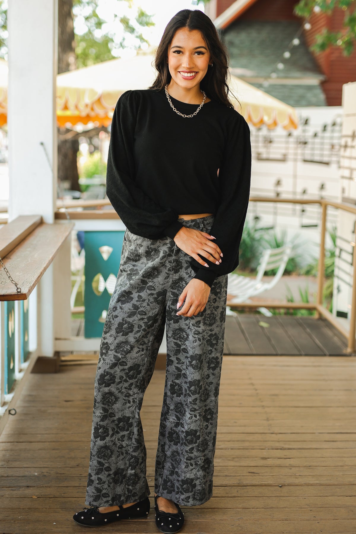 Woman wearing a black top and patterned pants on a wooden deck.