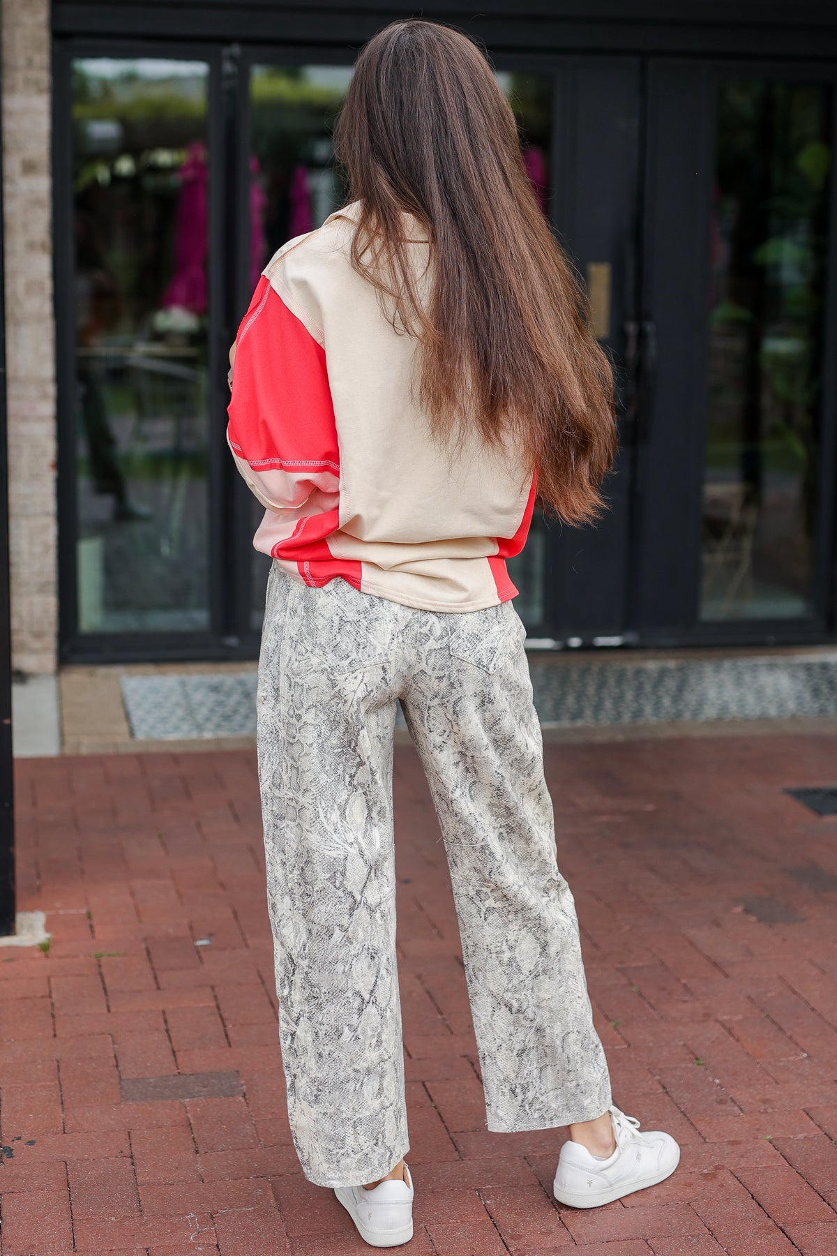 Woman wearing a beige and red top with patterned pants walking on a brick sidewalk.