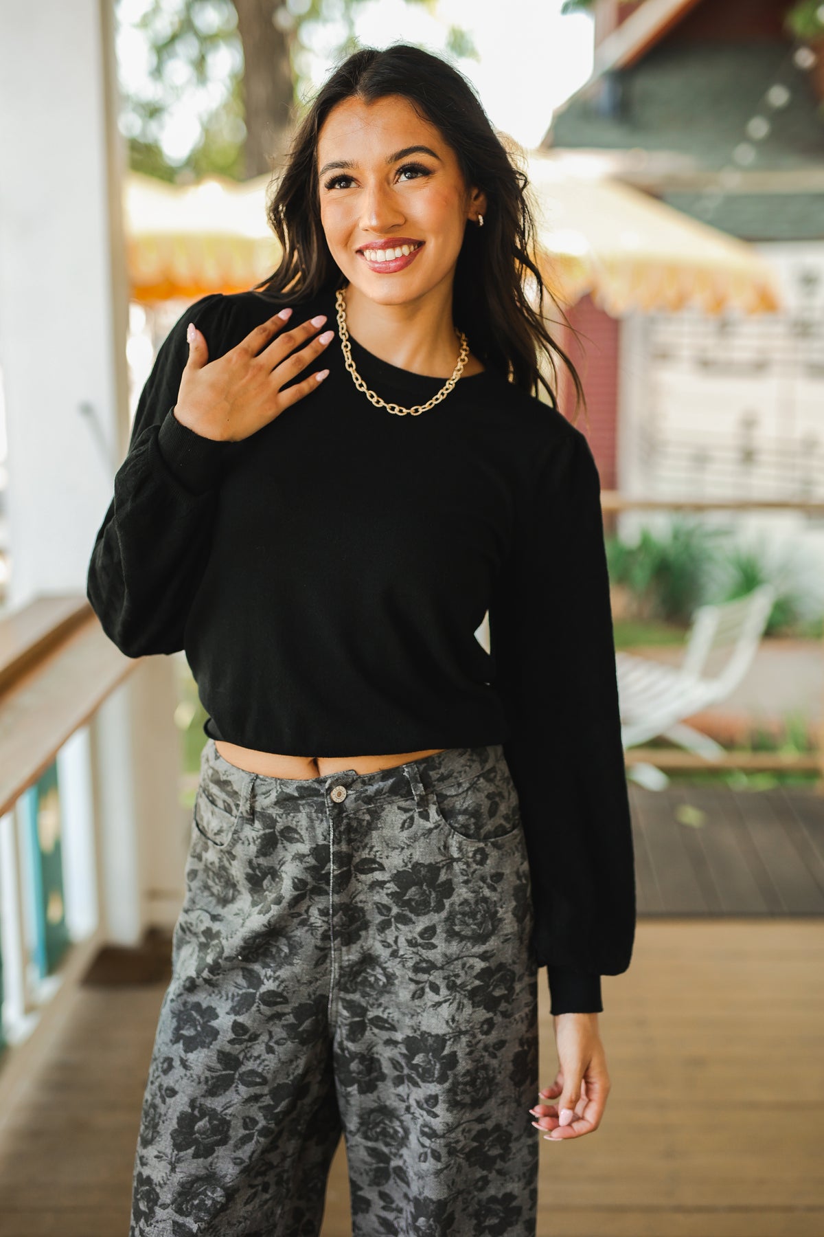 Woman wearing a black crop top and patterned pants on a porch.