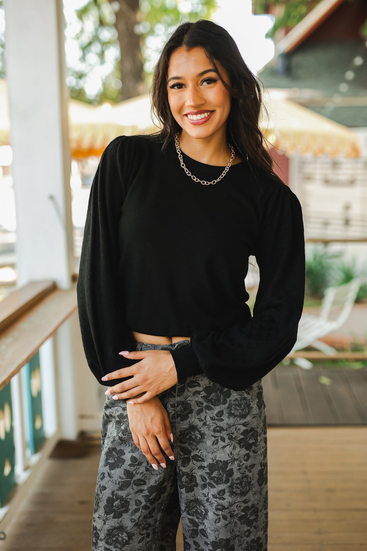 Woman wearing a black long-sleeve top and patterned pants standing outdoors.