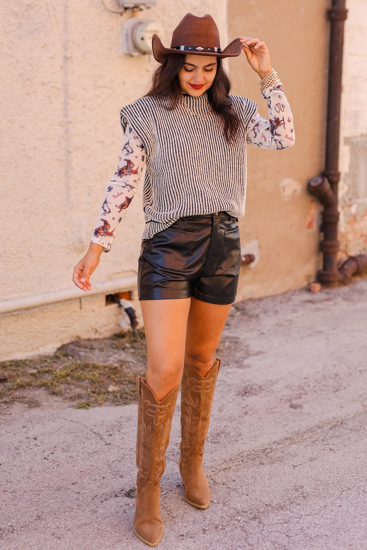 Woman wearing a striped sweater, leather shorts, and brown knee-high boots with a cowboy hat.