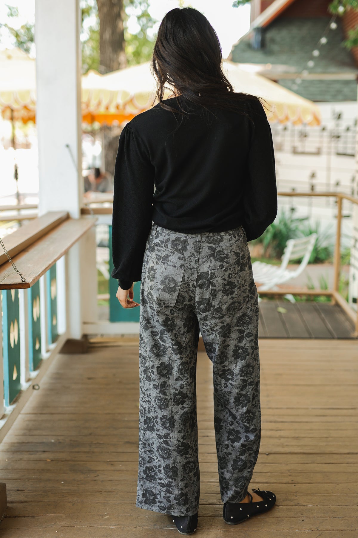 Person wearing a black top and patterned pants on a wooden deck.