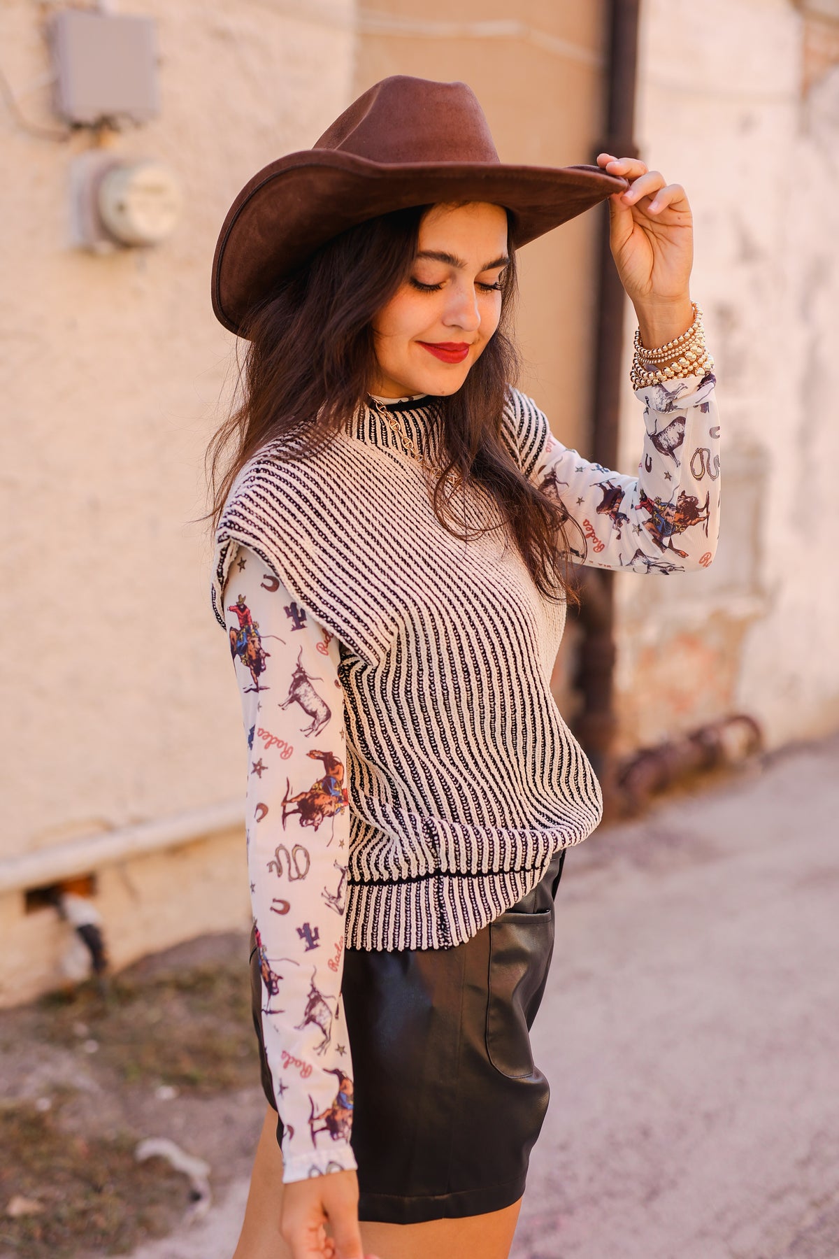 Woman wearing a patterned sweater and wide-brimmed hat outdoors.