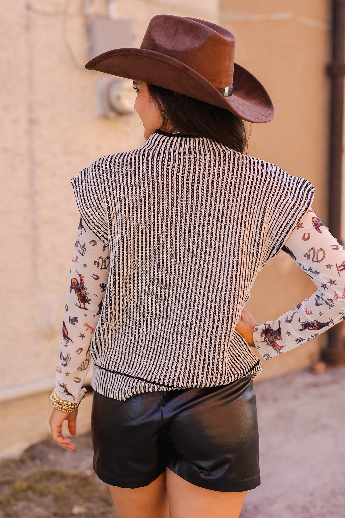 Person wearing a brown cowboy hat, patterned shirt, and black leather shorts.