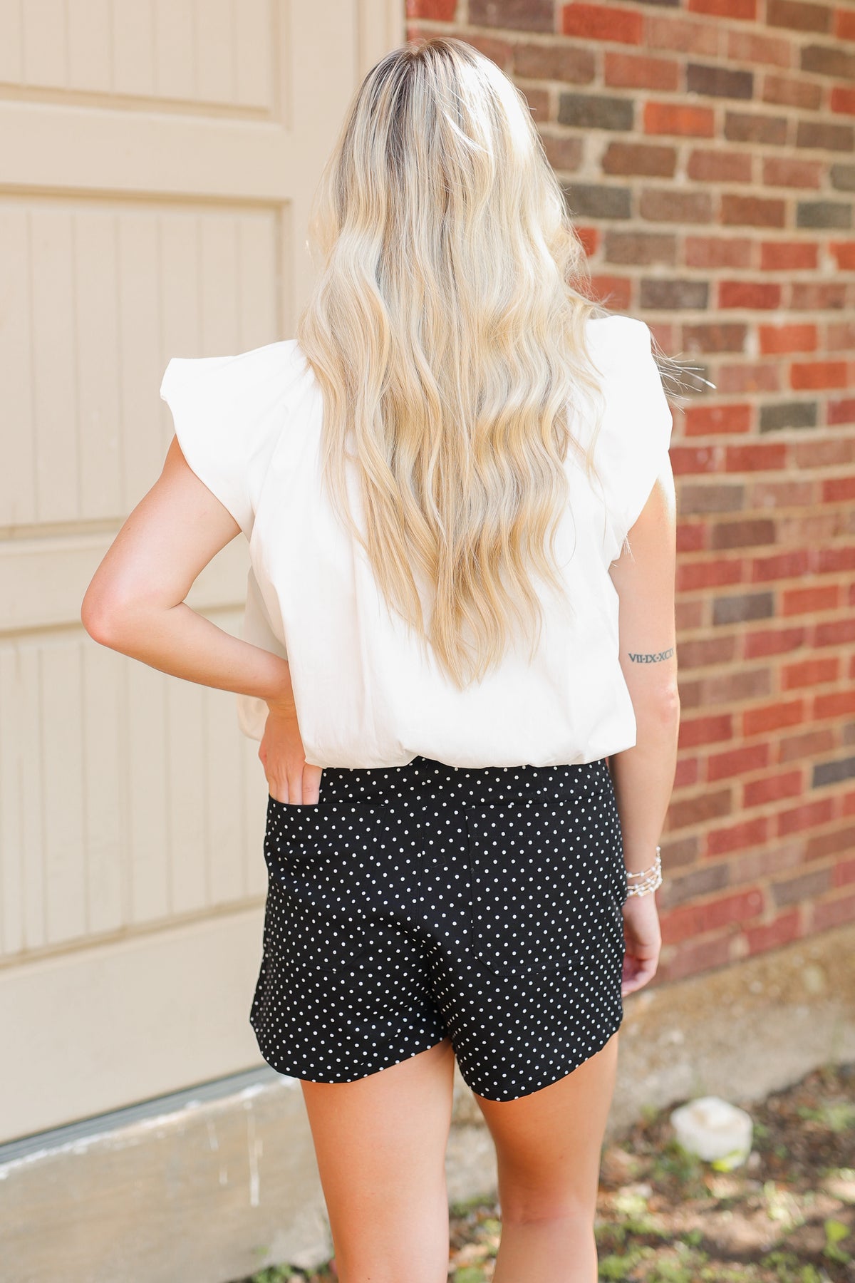Blonde model wearing a white top and black shorts with white dots.