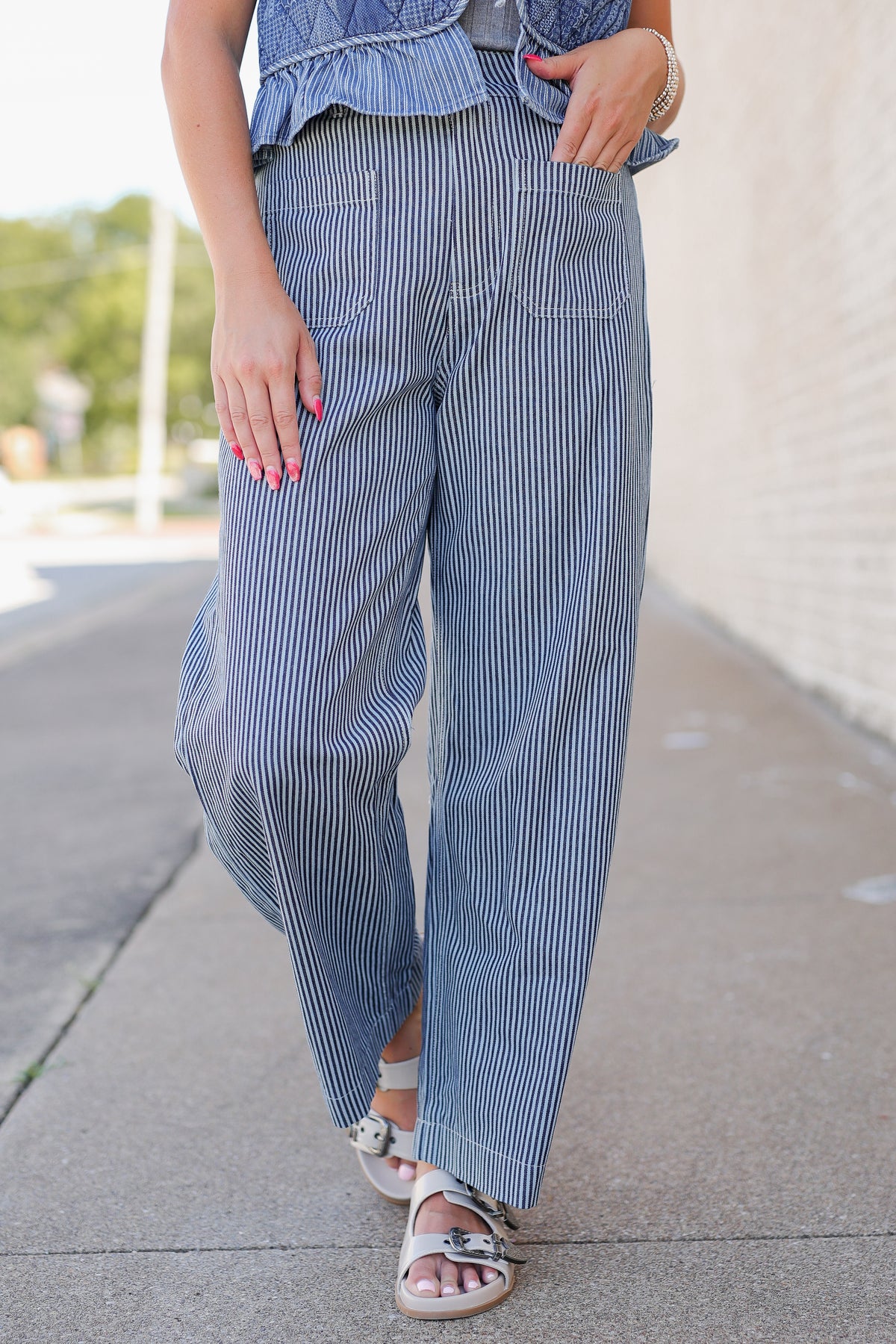 A person outdoors wearing wide-leg blue and white vertically striped pants, paired with a matching blue ruffled top and white slide sandals.