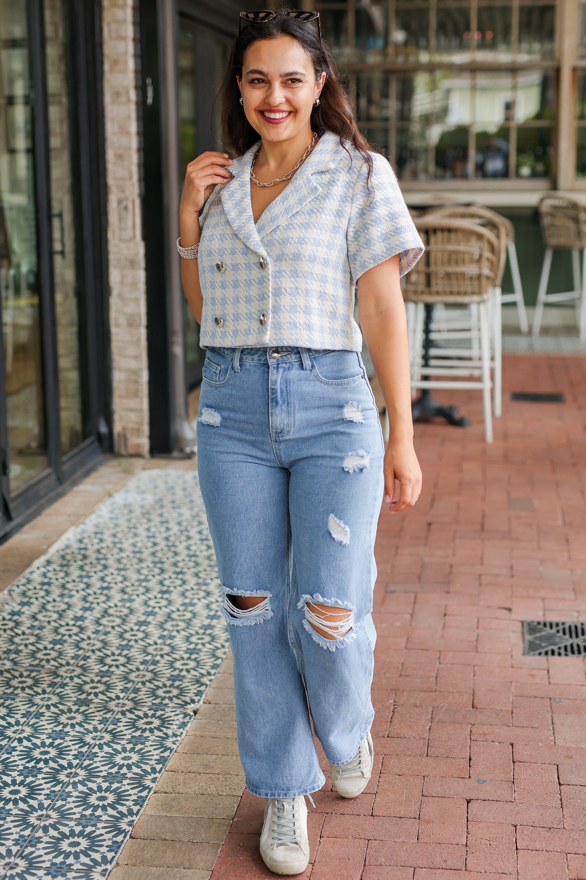 Woman wearing a checkered shirt and ripped jeans standing on a sidewalk.