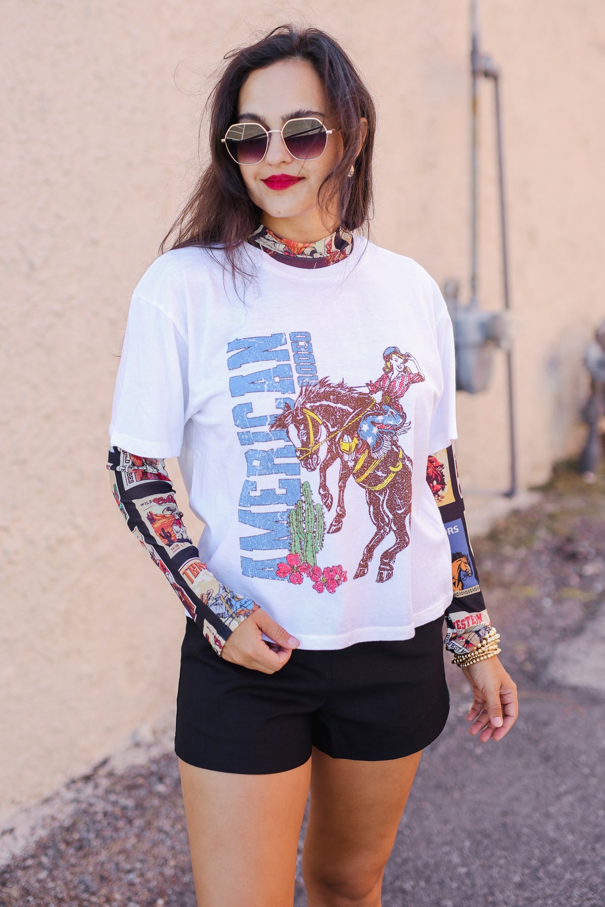 Woman wearing a graphic t-shirt with a horse and rider design, black shorts, and colorful sleeves.