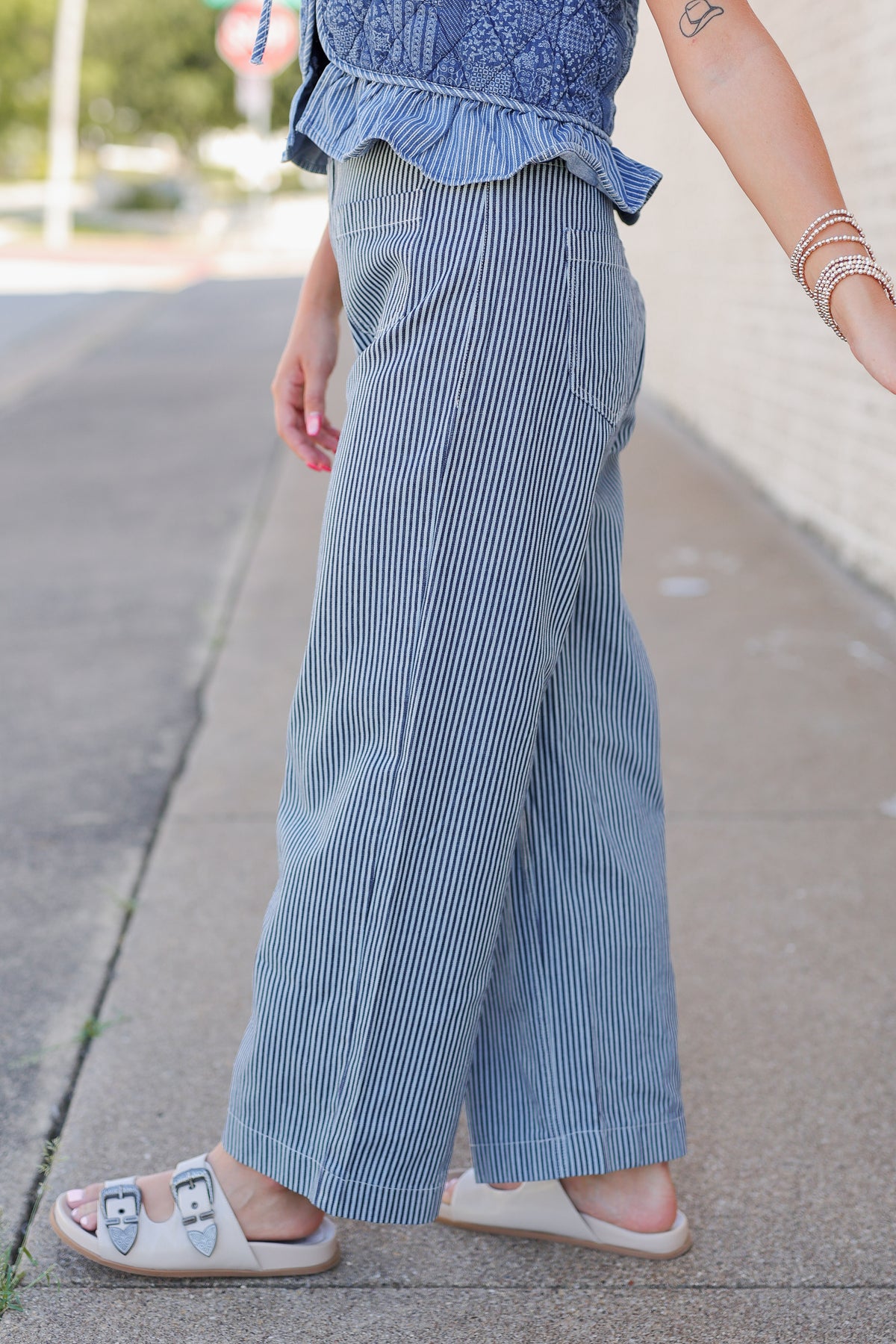 A person outdoors wearing wide-leg blue pinstriped pants with a matching blue ruffled top and beige slide sandals.