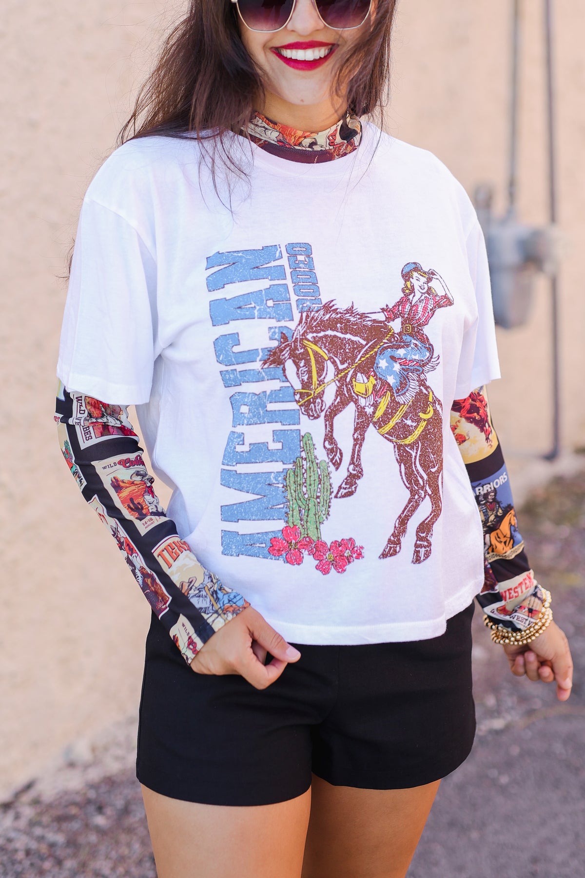 Person wearing a graphic t-shirt with a horse and cactus design, standing against a beige wall.