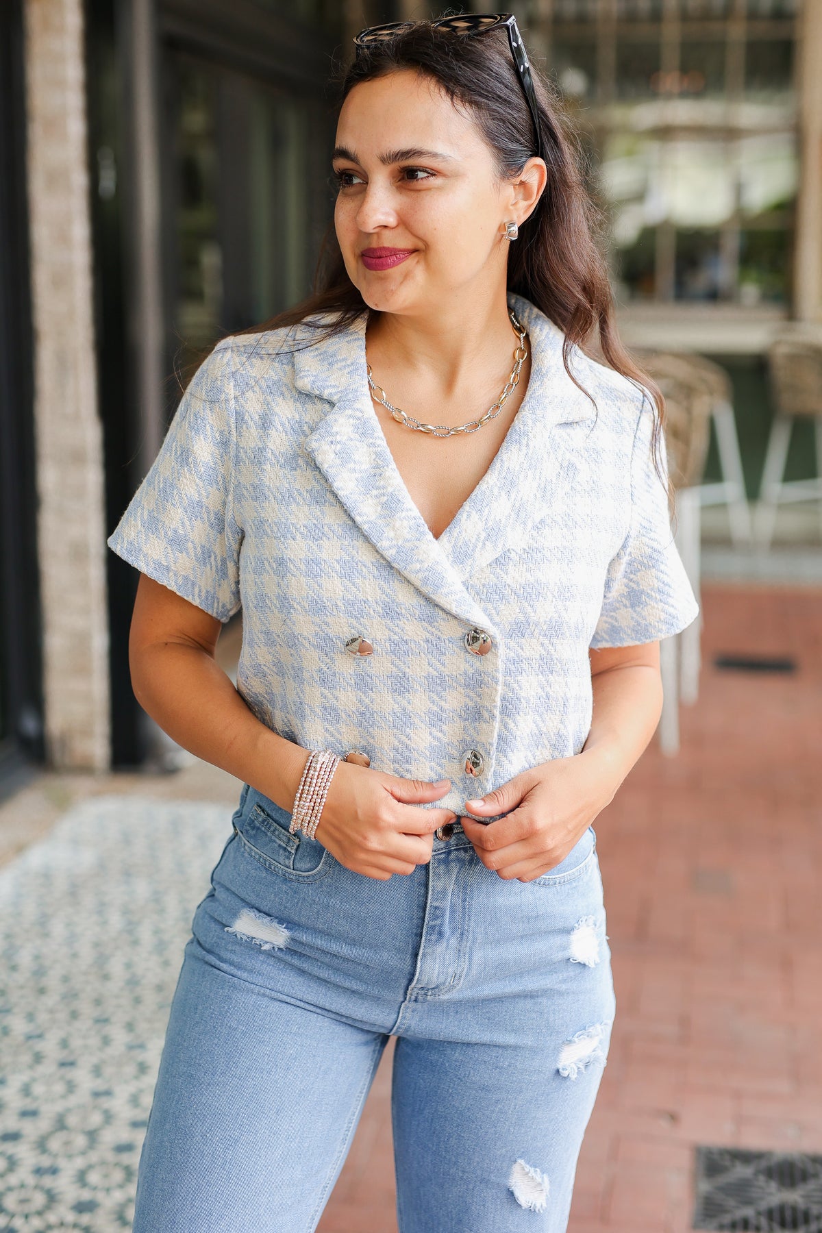 Woman wearing a light blue checkered blouse and ripped jeans outdoors.