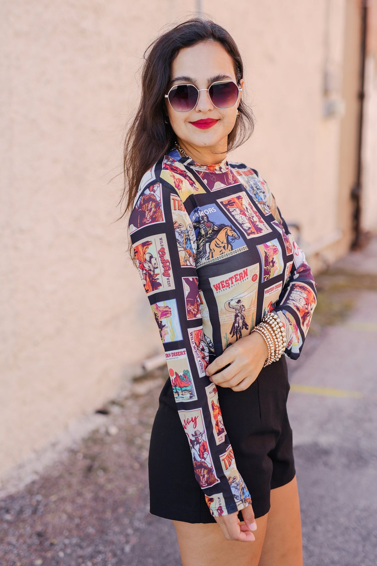 Woman wearing a colorful patterned shirt with a graphic design, standing against a beige wall.