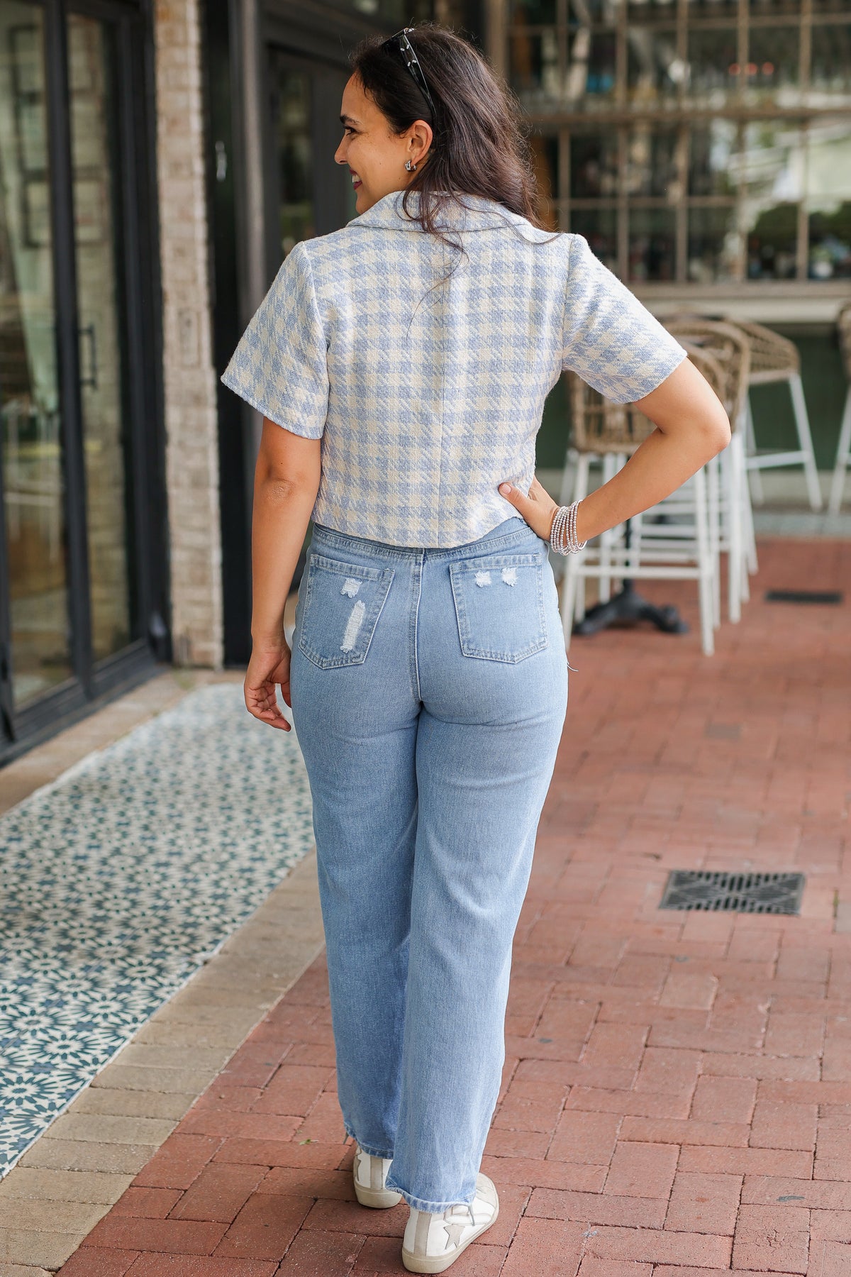 Woman wearing a checkered shirt and light blue jeans standing on a brick patio.