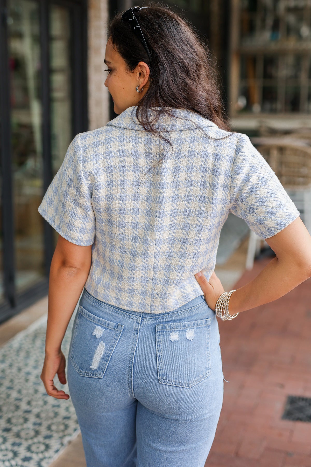 Person wearing a light blue checkered shirt and jeans in an outdoor setting.