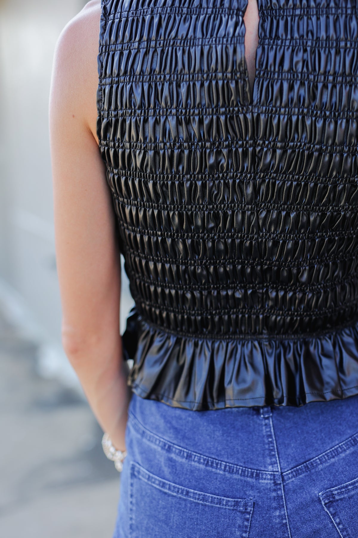 Black smocked top with ruffled hem worn by a person, blurred background