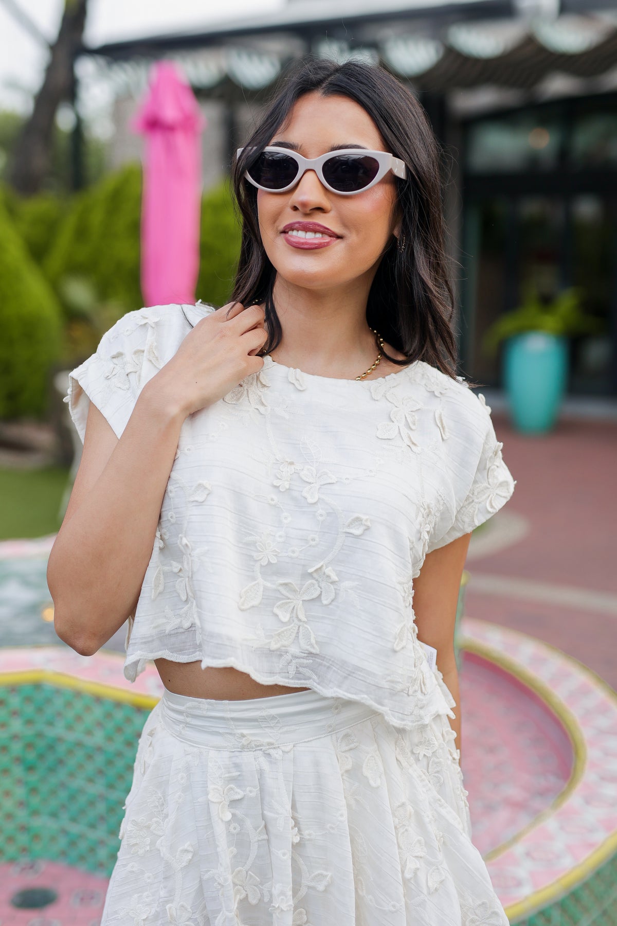 Woman wearing a white lace outfit with sunglasses outdoors.