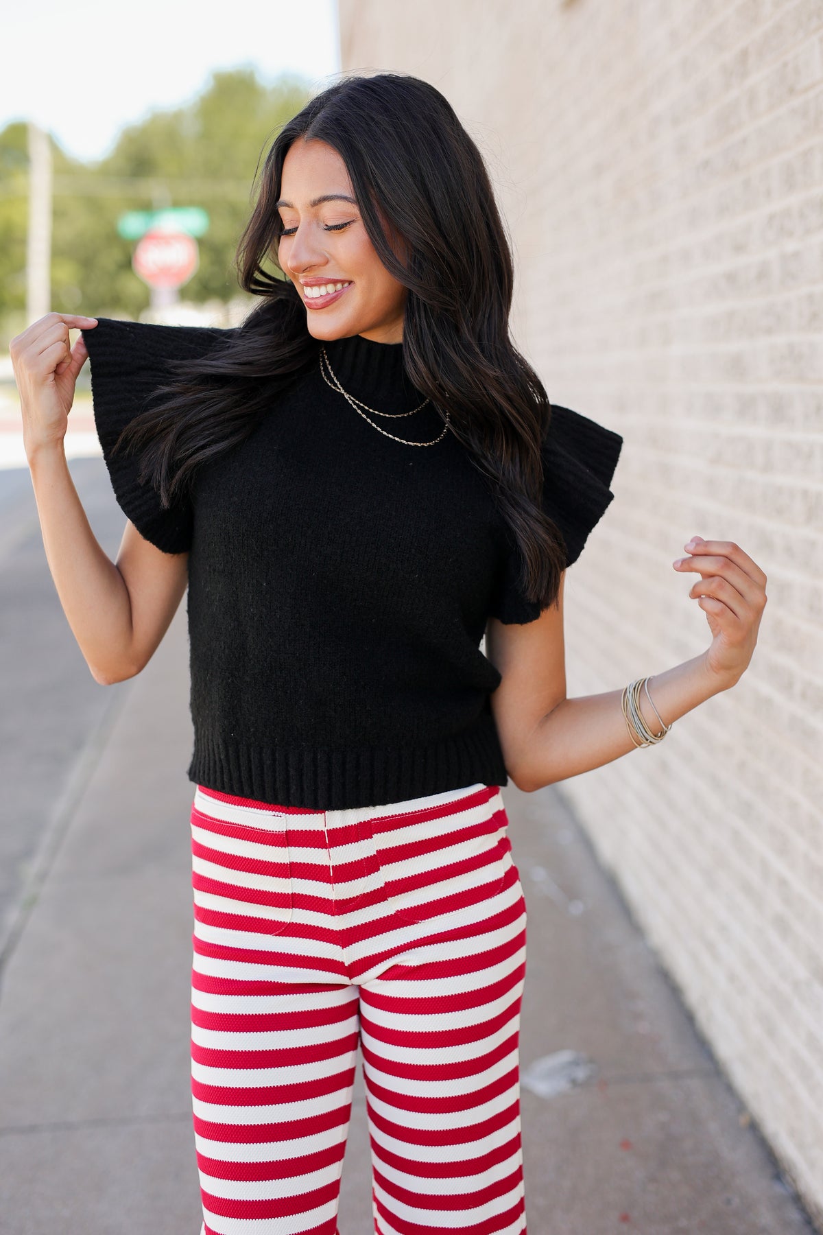 Model wearing a lightweight black sweater with red and white striped pants standing outdoors.