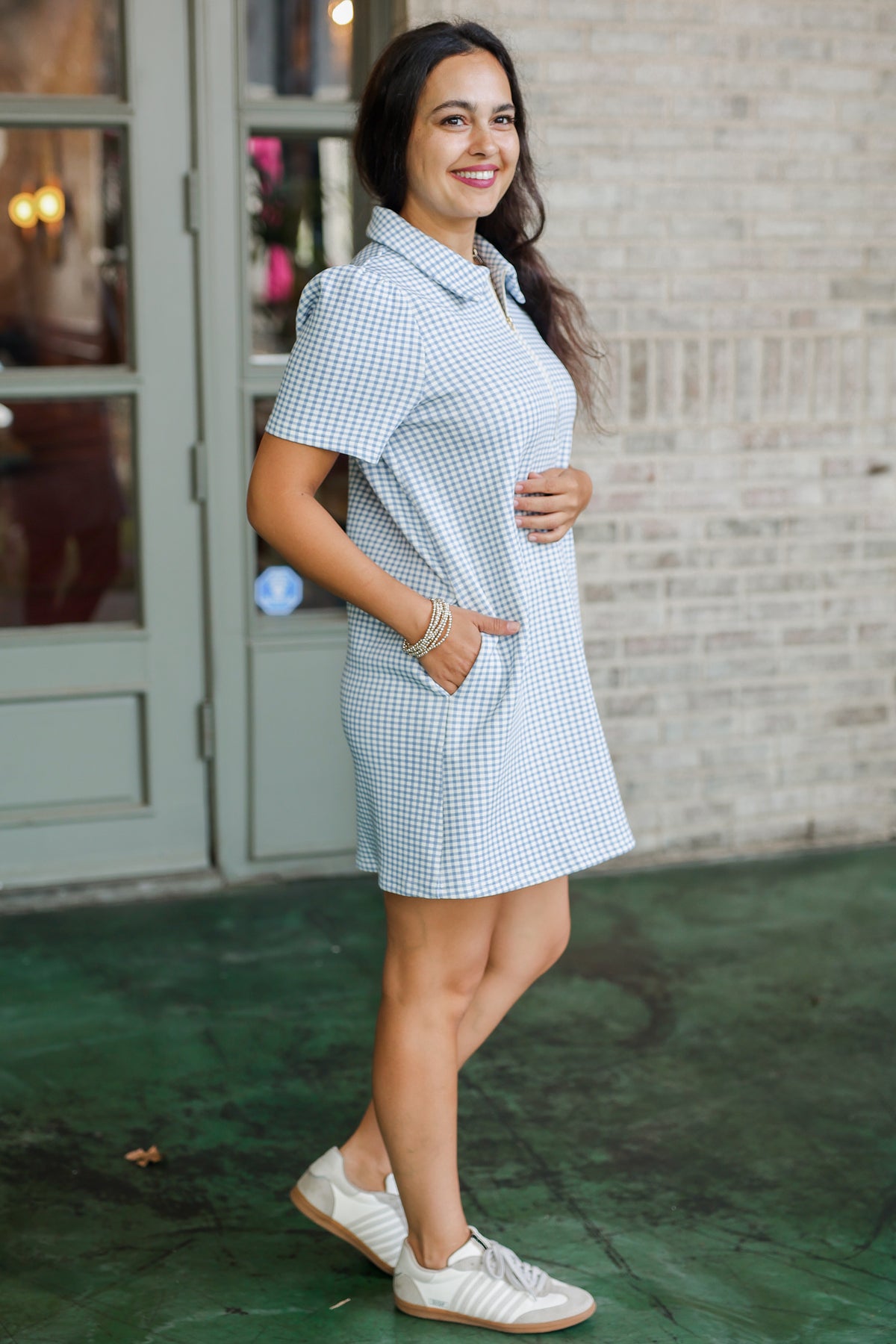 Woman wearing a checkered dress standing in front of a brick wall.