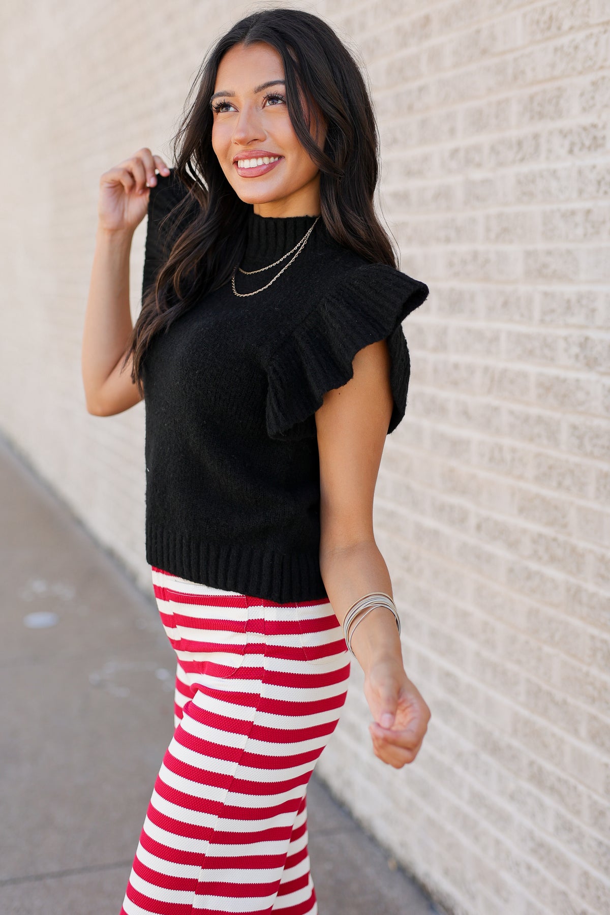 Model wearing a lightweight black sweater with red and white striped pants standing outdoors.