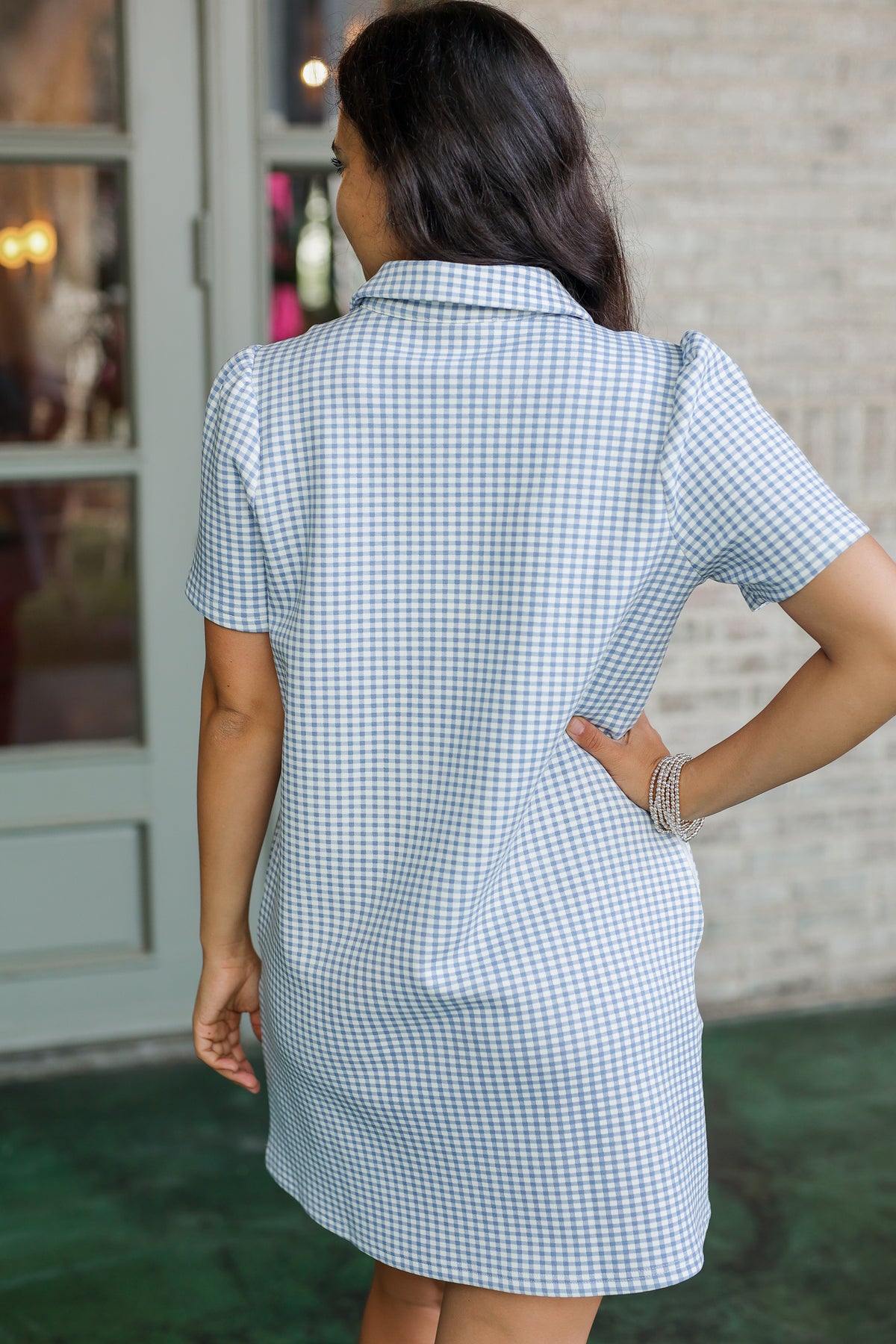 Woman wearing a blue and white checkered dress with a blurred indoor background