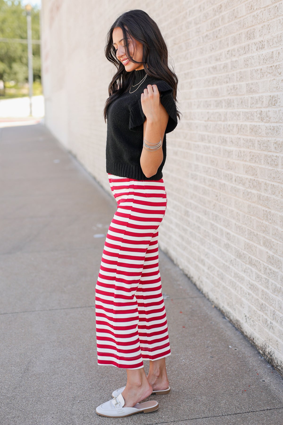 Model wearing a lightweight black sweater with red and white striped pants standing outdoors.