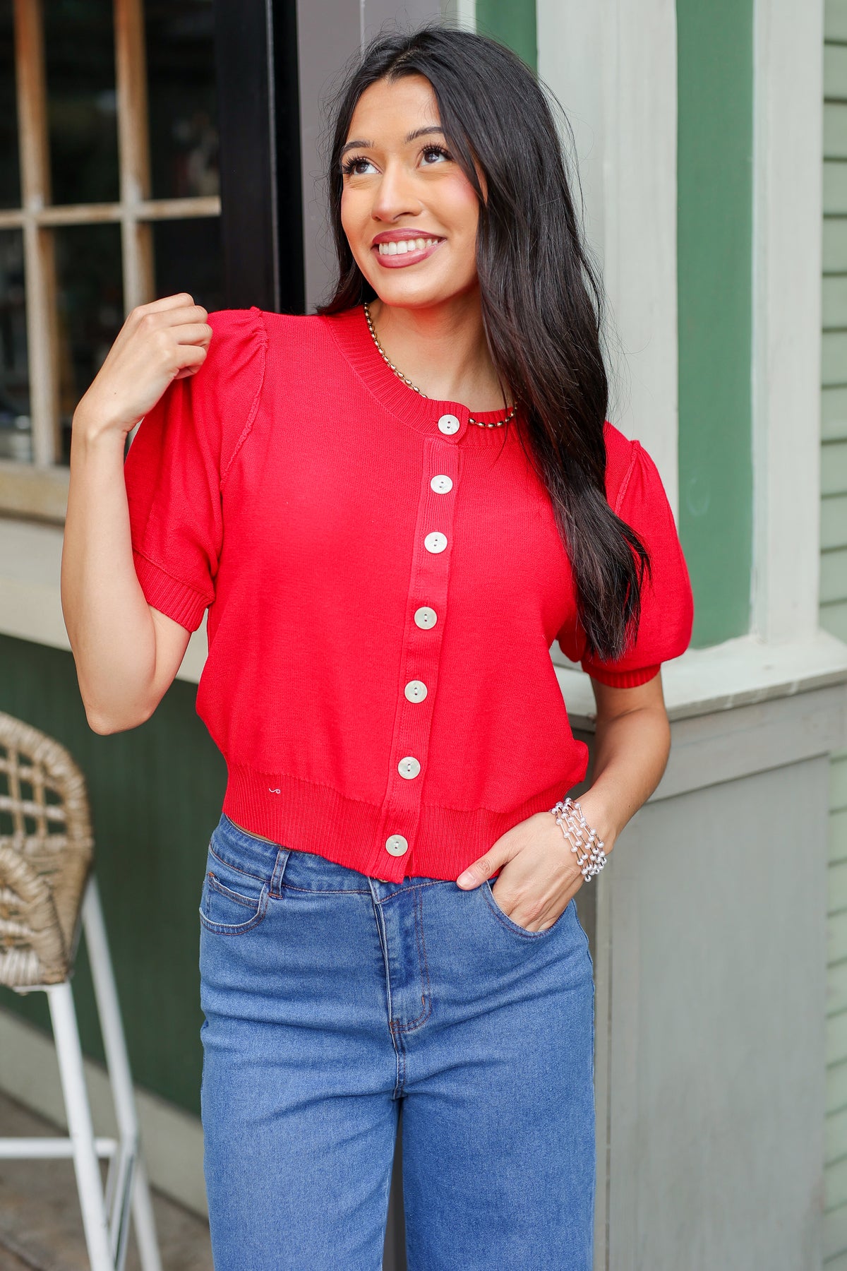 Woman wearing a red cardigan and blue jeans standing outdoors.