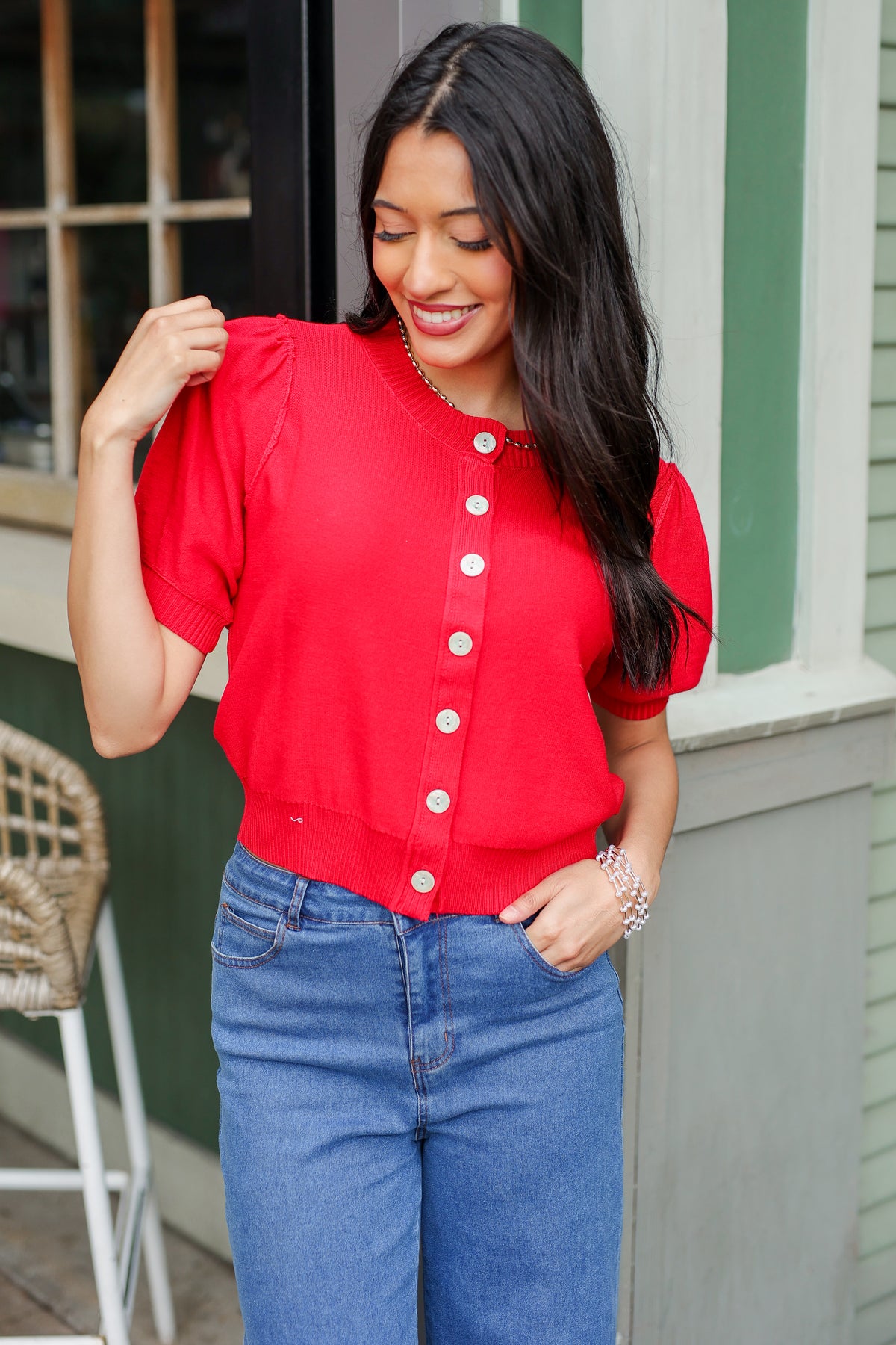 Woman wearing a red blouse with white buttons and blue jeans, standing outdoors.