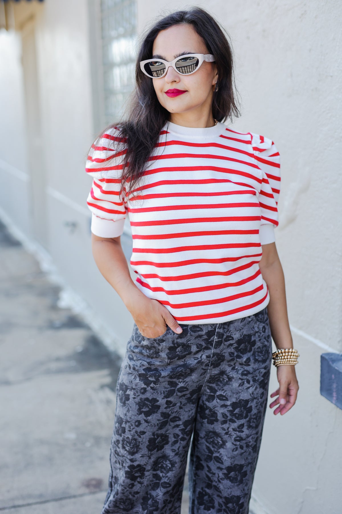 Woman wearing a red and white striped shirt with floral pants against a light-colored wall.