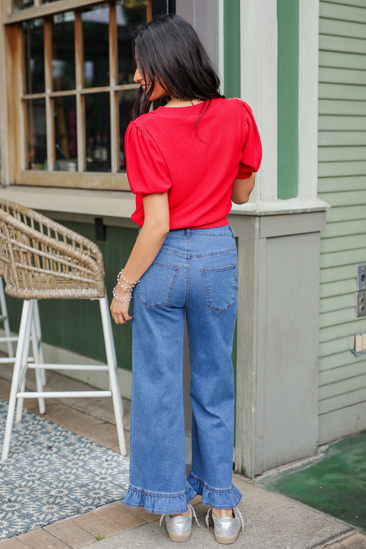 Woman in a red top and blue jeans standing on a porch.