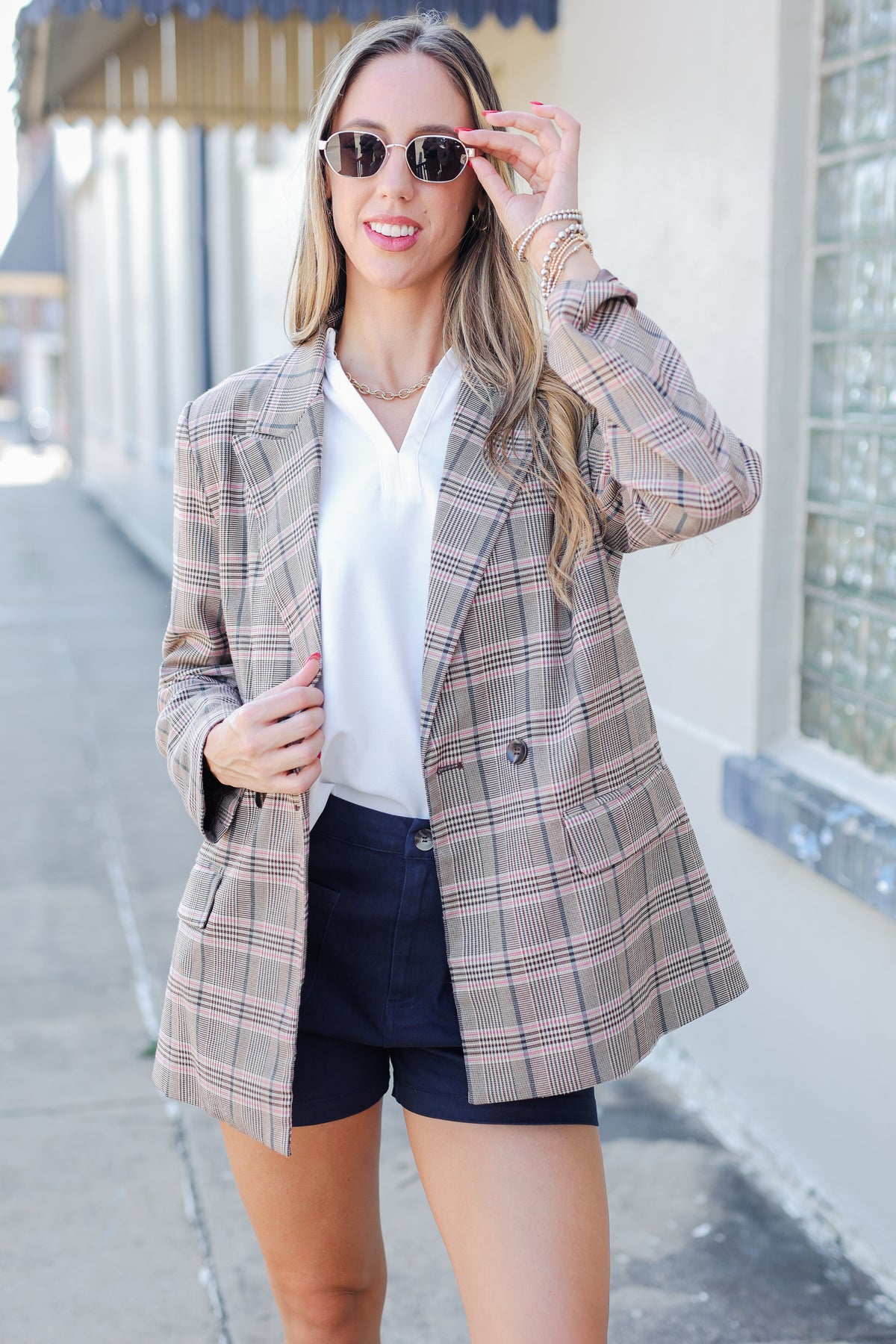 Woman wearing a plaid blazer over a white shirt and black shorts, standing outdoors.