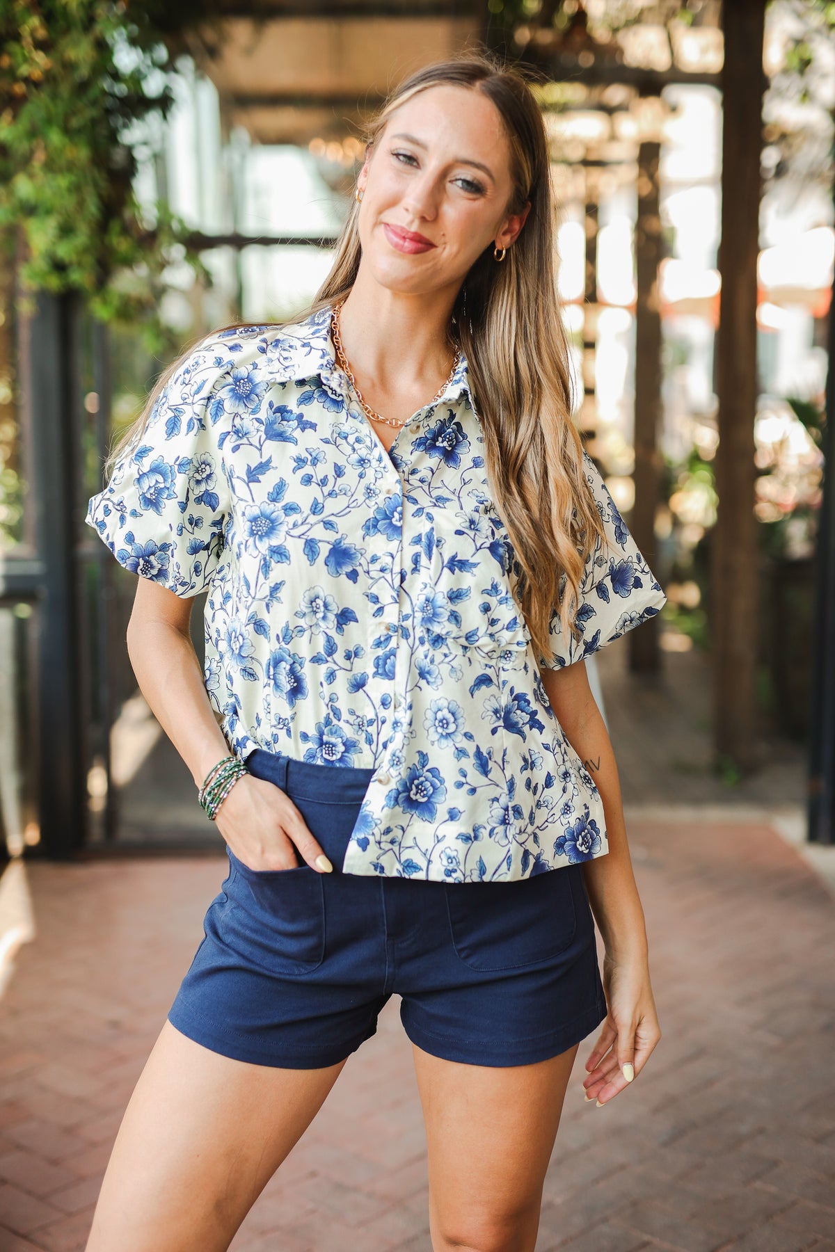 Woman wearing a floral shirt and navy shorts standing outdoors.