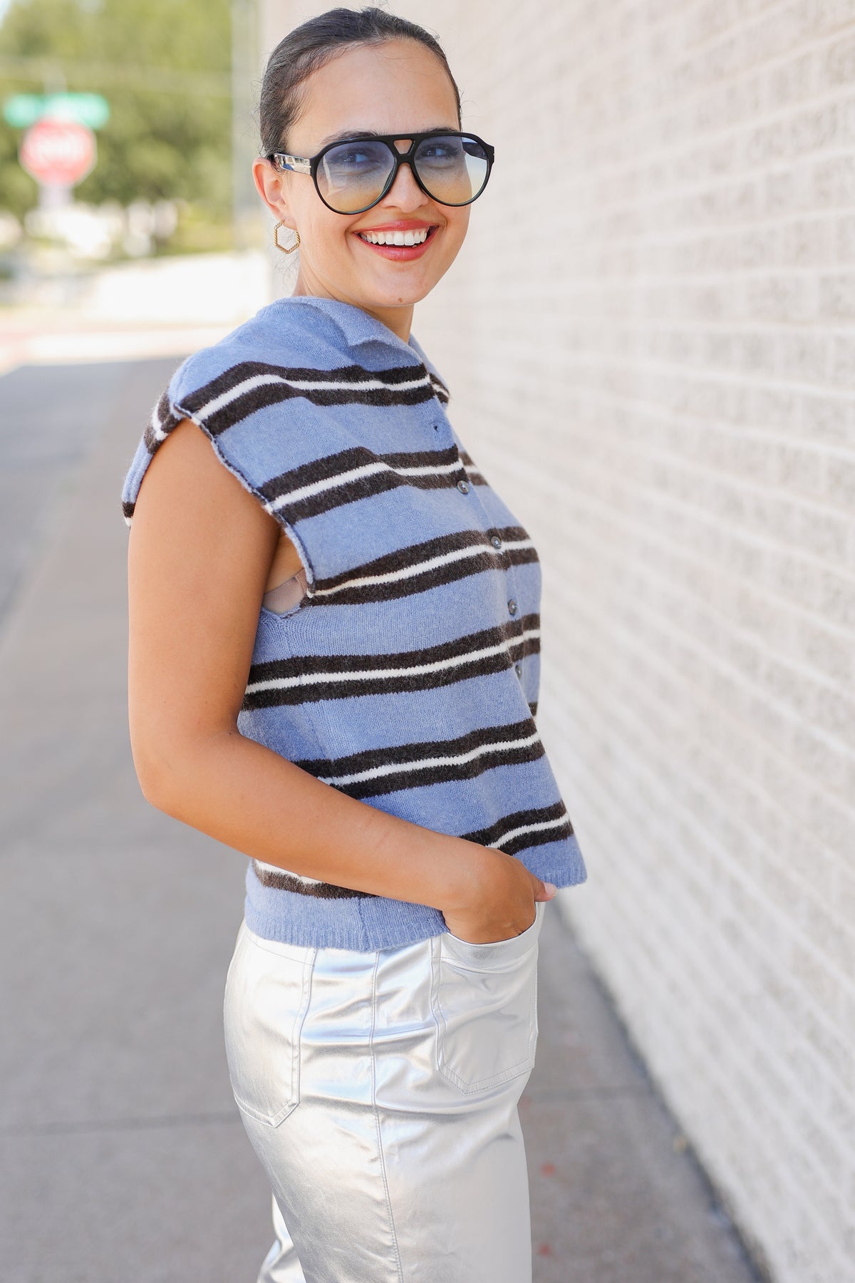 Woman standing outside wearing a blue striped sweater vest and metallic silver pants.