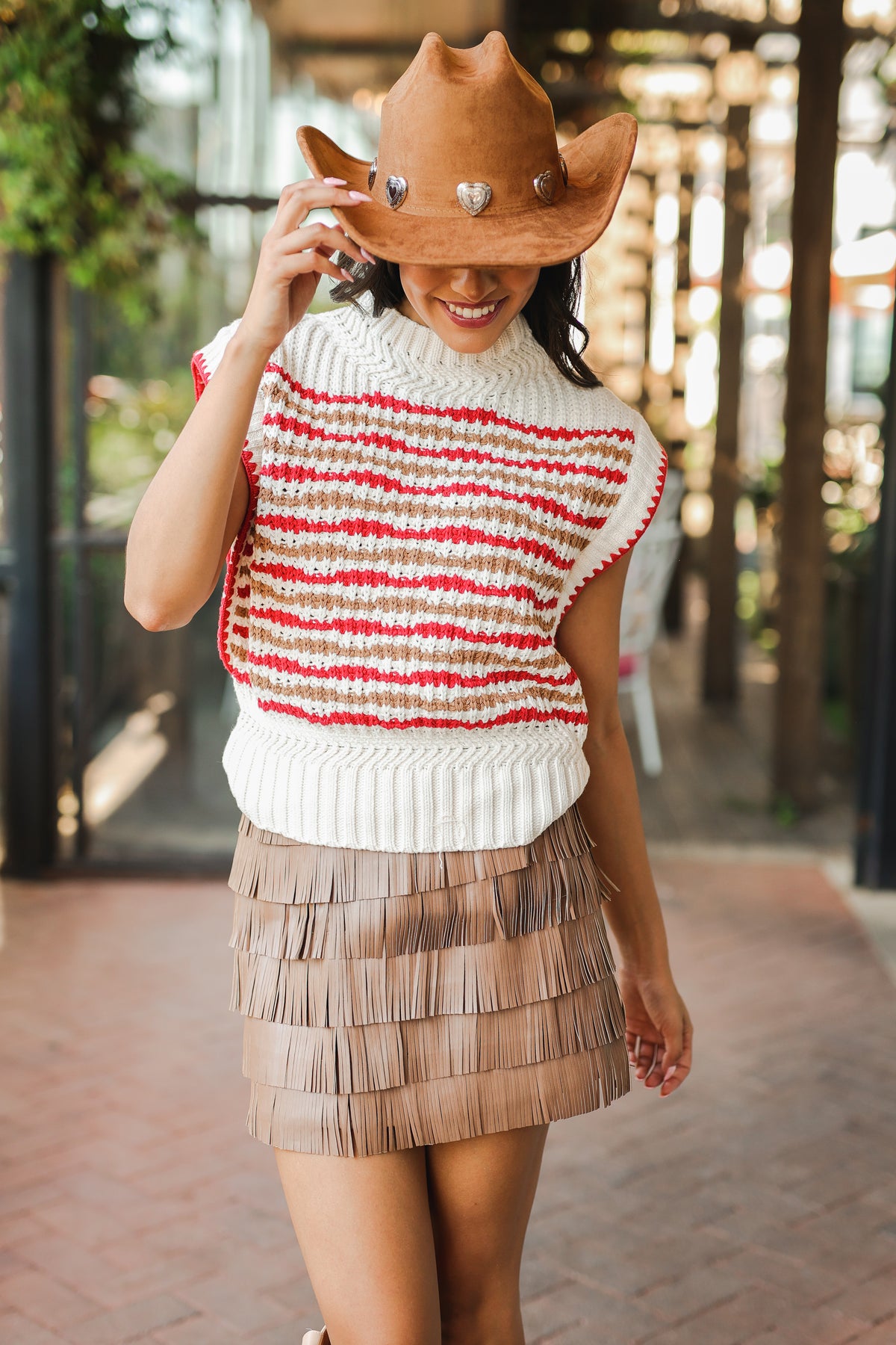 Woman wearing a striped sweater vest and tiered skirt with a cowboy hat outdoors.