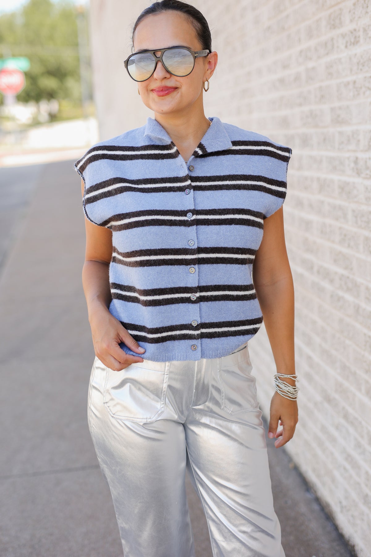 Woman standing outside wearing a blue striped sweater vest and metallic silver pants.
