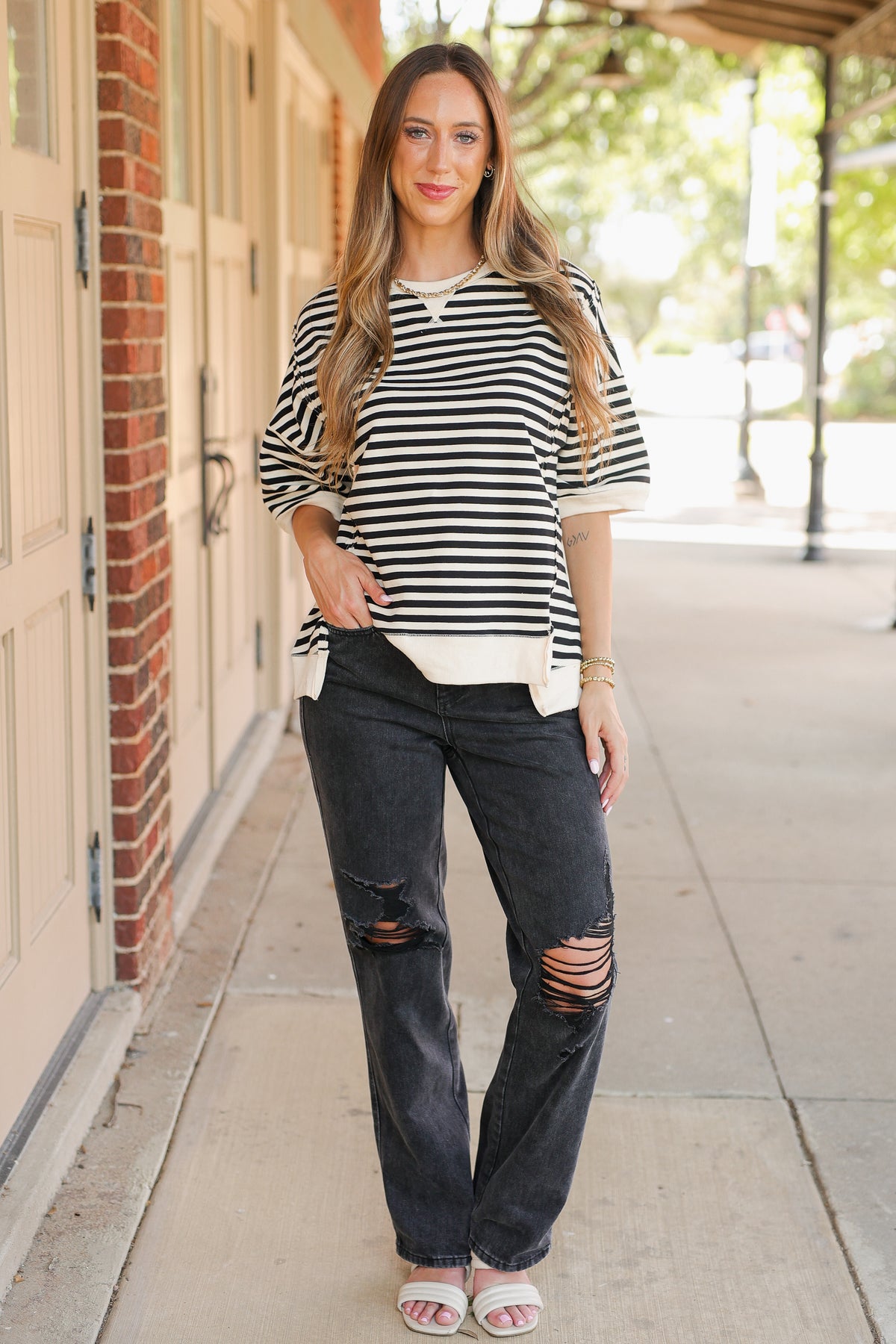 Woman wearing a striped shirt and ripped jeans standing on a sidewalk.