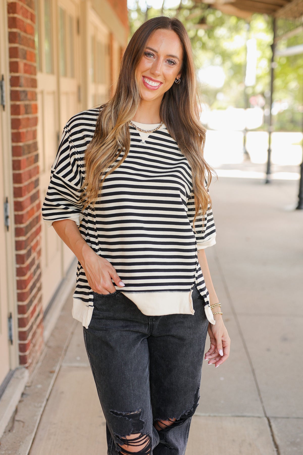 Woman wearing a black and white striped shirt and ripped jeans on a sidewalk.